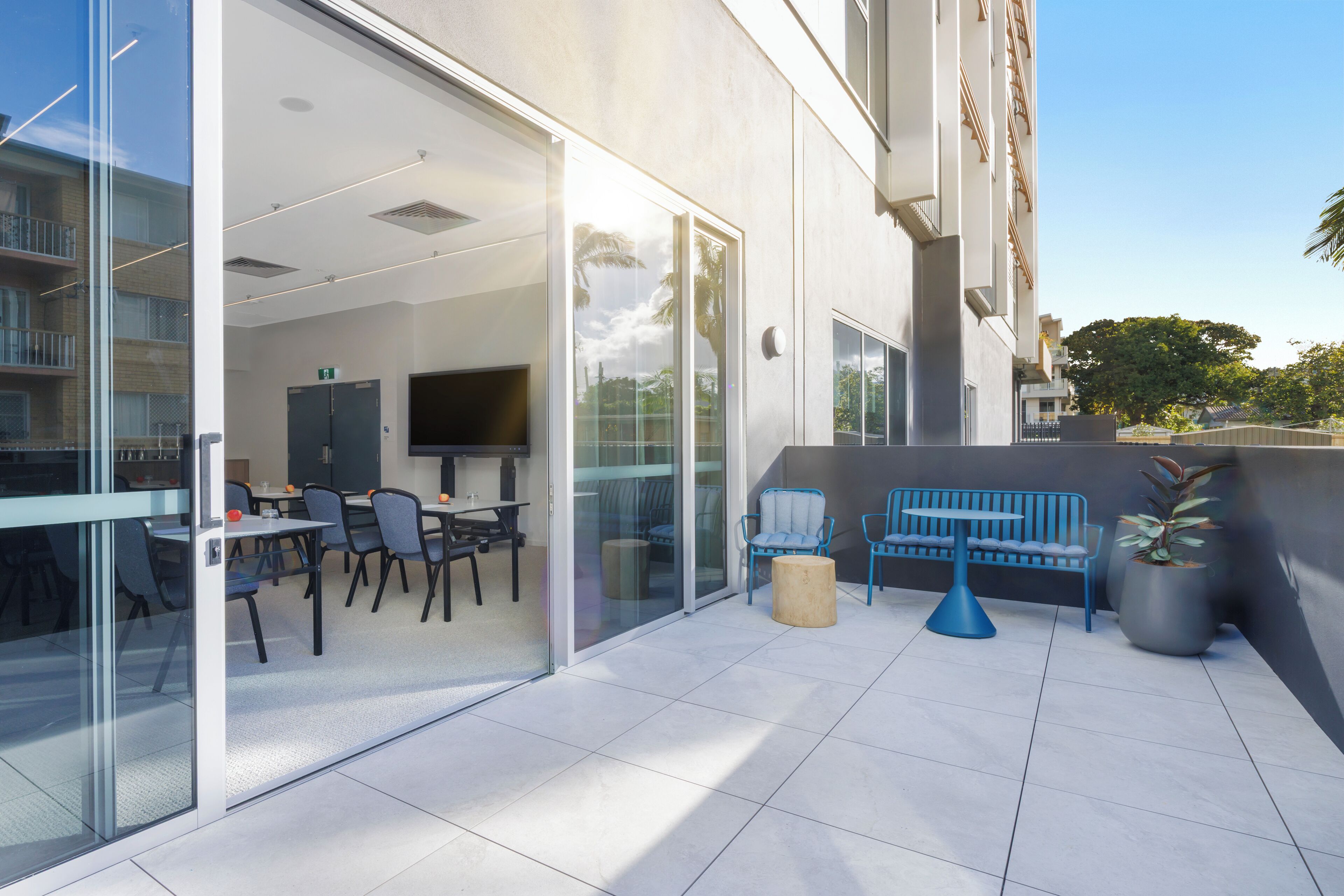An outdoor patio area with a seating arrangement, a television, and a glass door leading to an interior space.