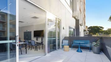 Un espace extérieur aménagé en terrasse, avec des sièges, un téléviseur et une porte vitrée donnant sur un espace intérieur.