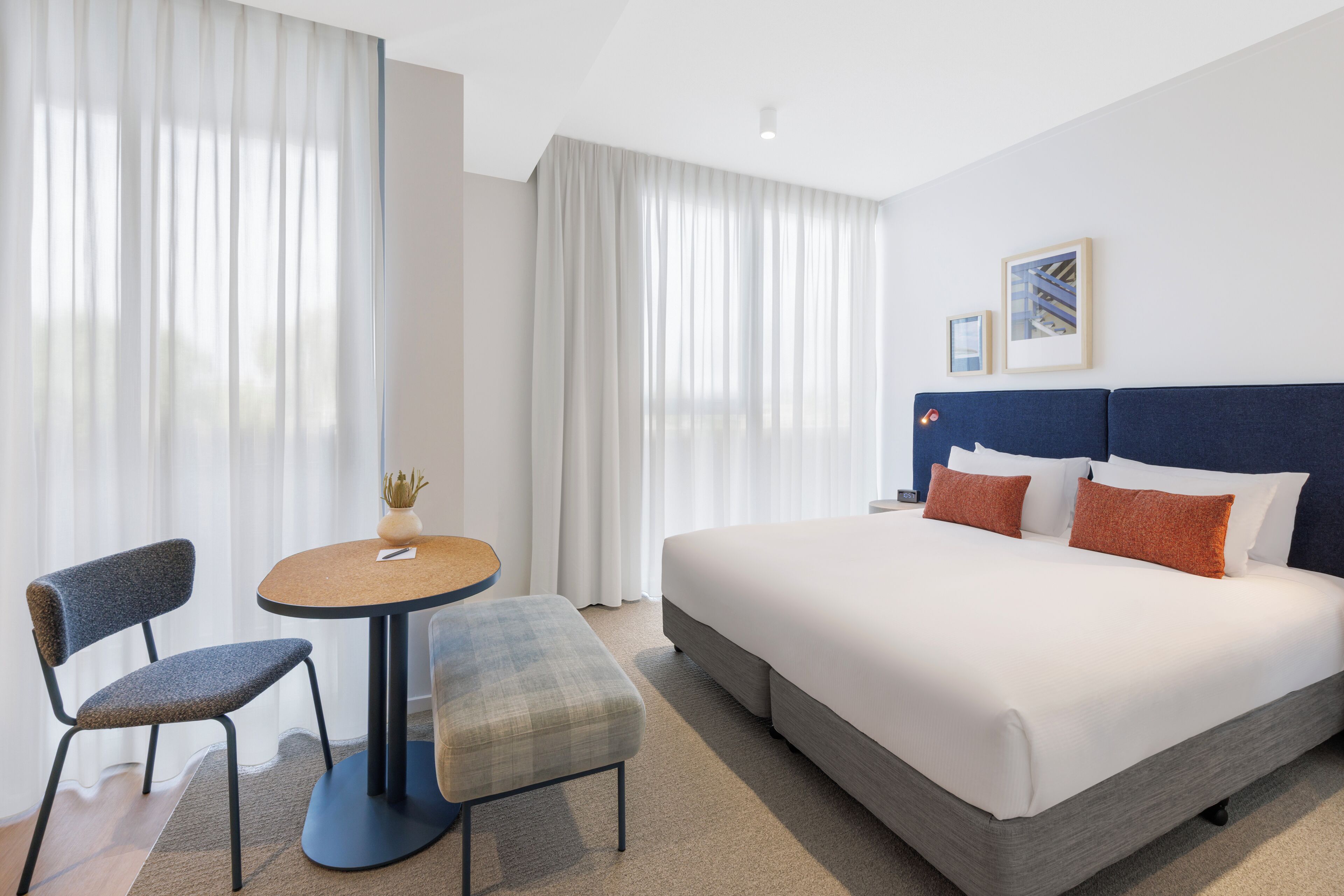 A hotel room with a bed, a desk, a chair, and a window with curtains.