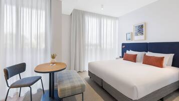A hotel room with a bed, a desk, a chair, and a window with curtains.