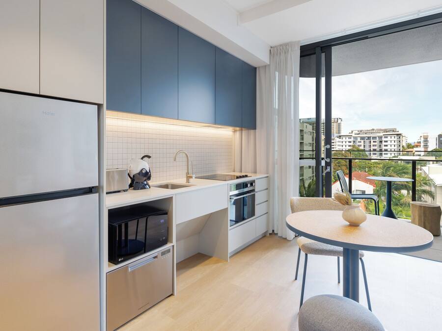 A modern kitchen with a refrigerator, microwave, and oven. There is a dining area with a table and chairs.