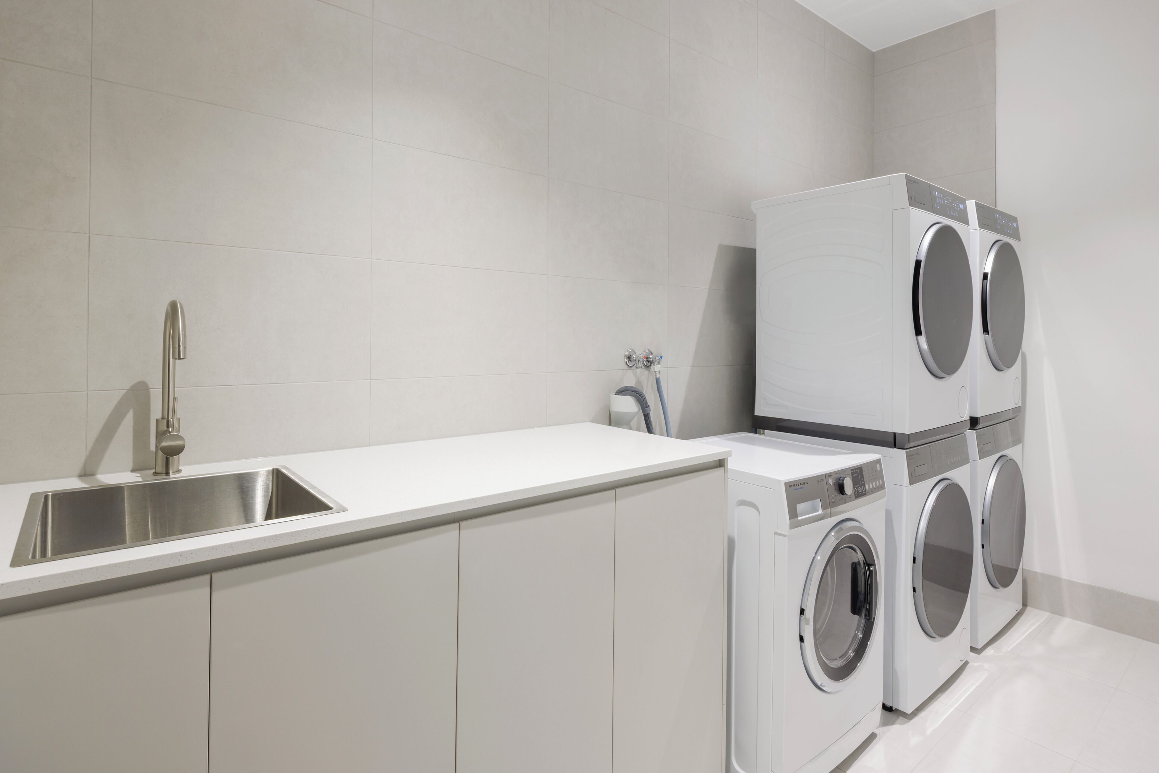 A modern kitchen with a stainless steel sink, white cabinets, and a built-in washing machine.
