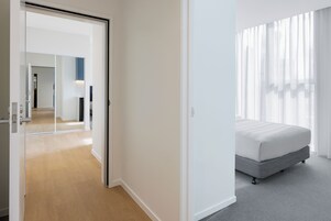 A modern hotel room with a bed, a walk-in closet, and a view of the city through sheer curtains.