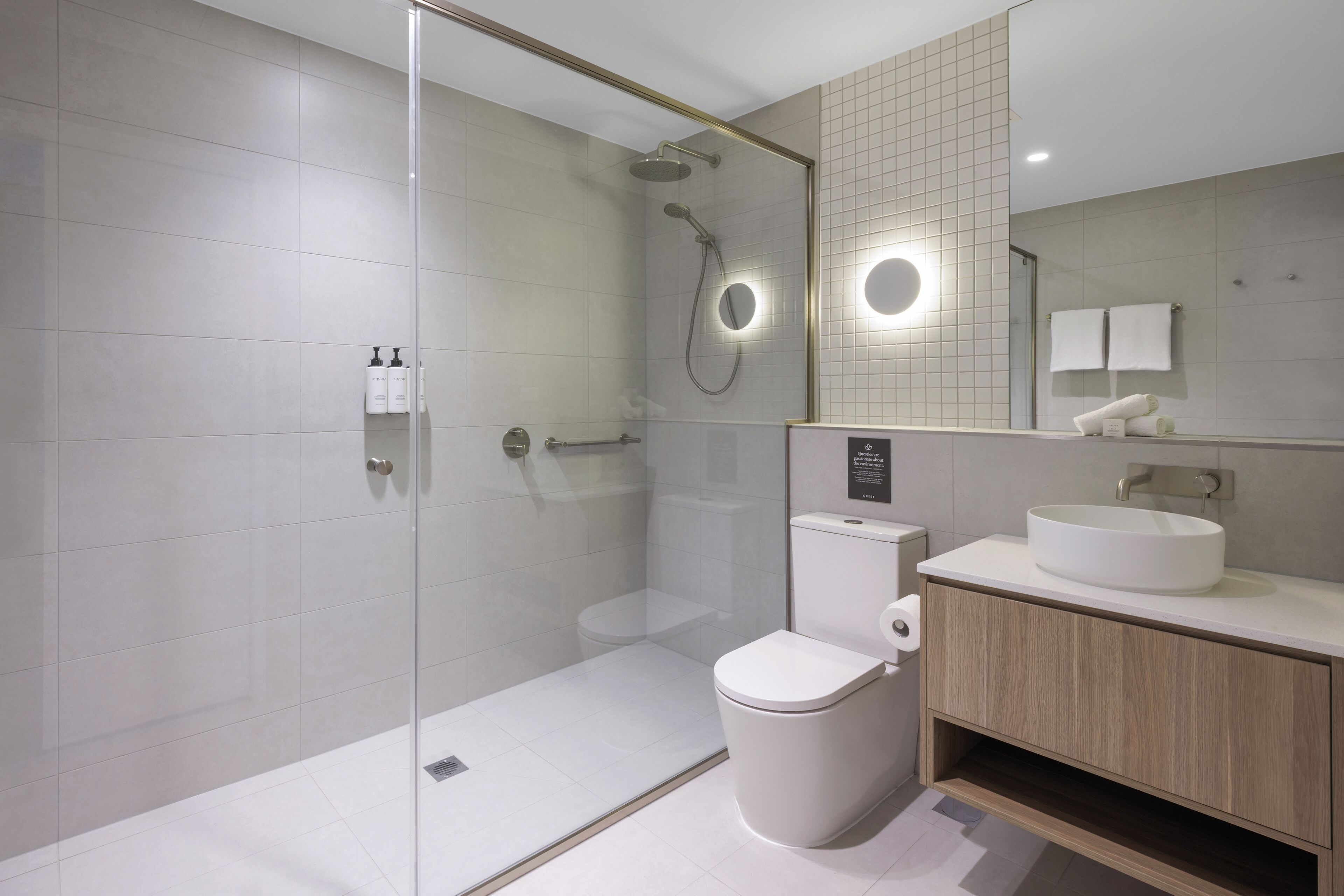 A modern bathroom with a glass-enclosed shower, a toilet, a sink, and a mirror.