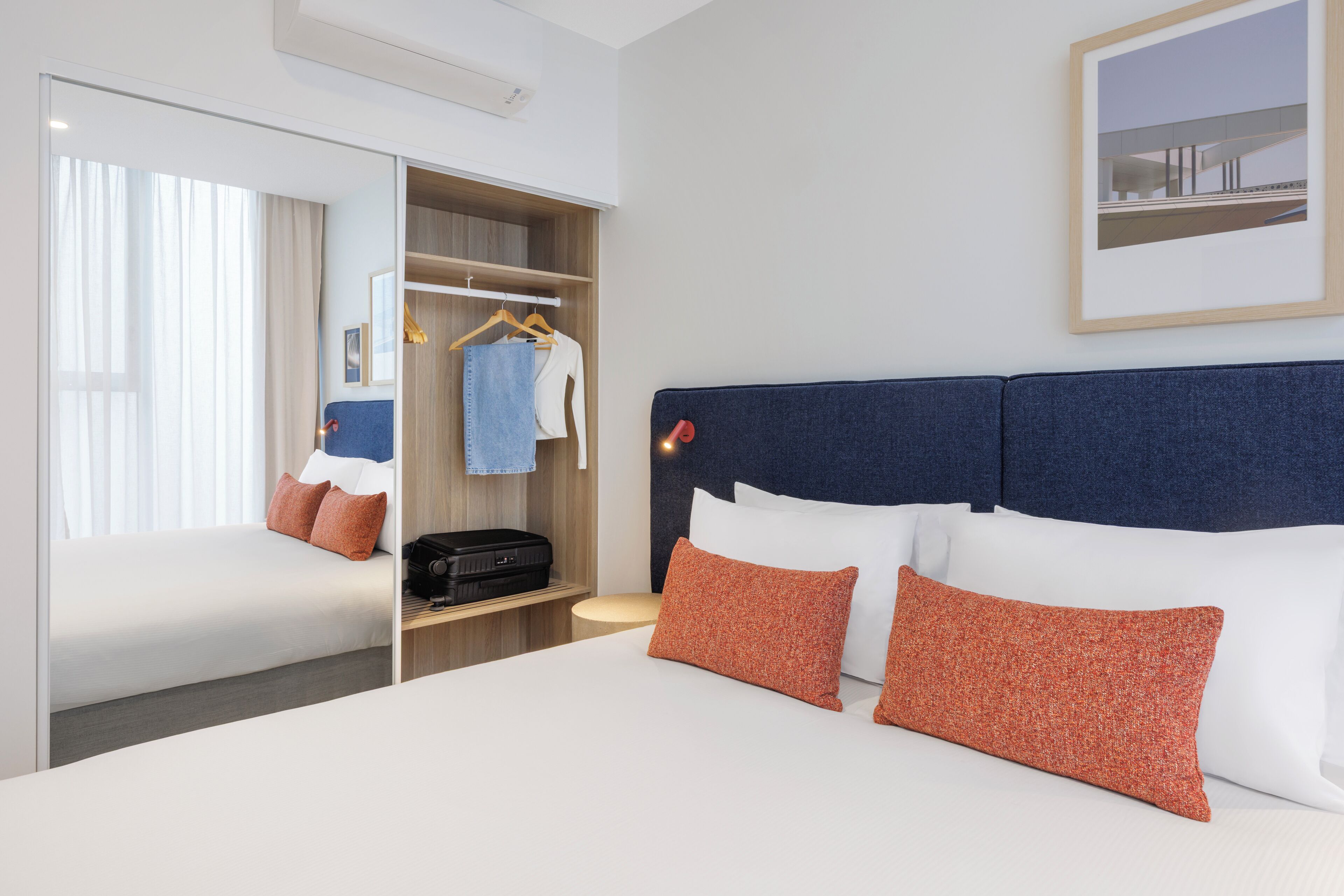 A hotel room with a bed, a wardrobe, a suitcase, and a framed picture on the wall.