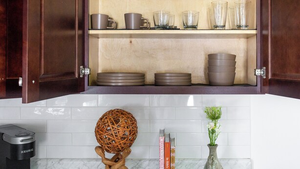 Una cocina con armarios de madera, encimera de mármol, cafetera, esfera de mimbre decorativa y un florero con flores.