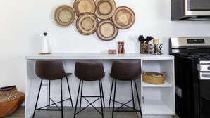 Una cocina con encimera blanca, tres taburetes de bar, un microondas y una estufa.