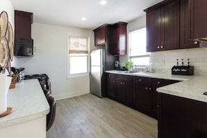 A modern kitchen with dark wood cabinets, a stainless steel refrigerator, a marble countertop, and a coffee bar.
