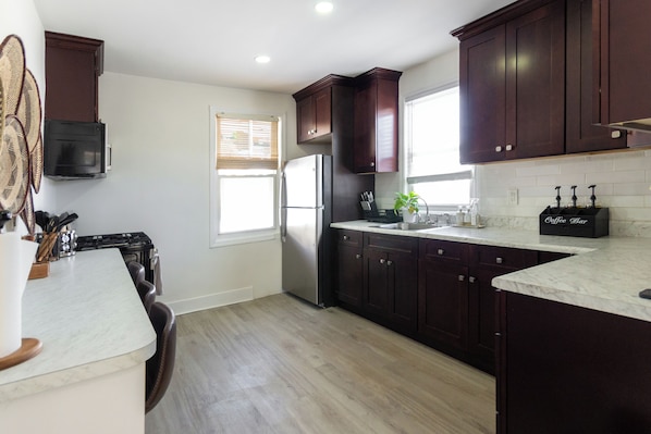 Una cocina moderna con armarios de madera oscura, un refrigerador de acero inoxidable, una encimera de mármol y una barra de café.