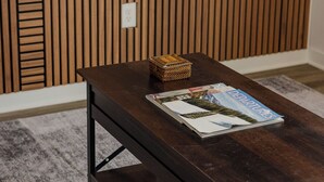 Ein dunkler Holztisch mit einer Zeitschrift und einem gewebten Korb darauf, platziert in einem Raum mit grauem Teppich und Holzpaneelen.