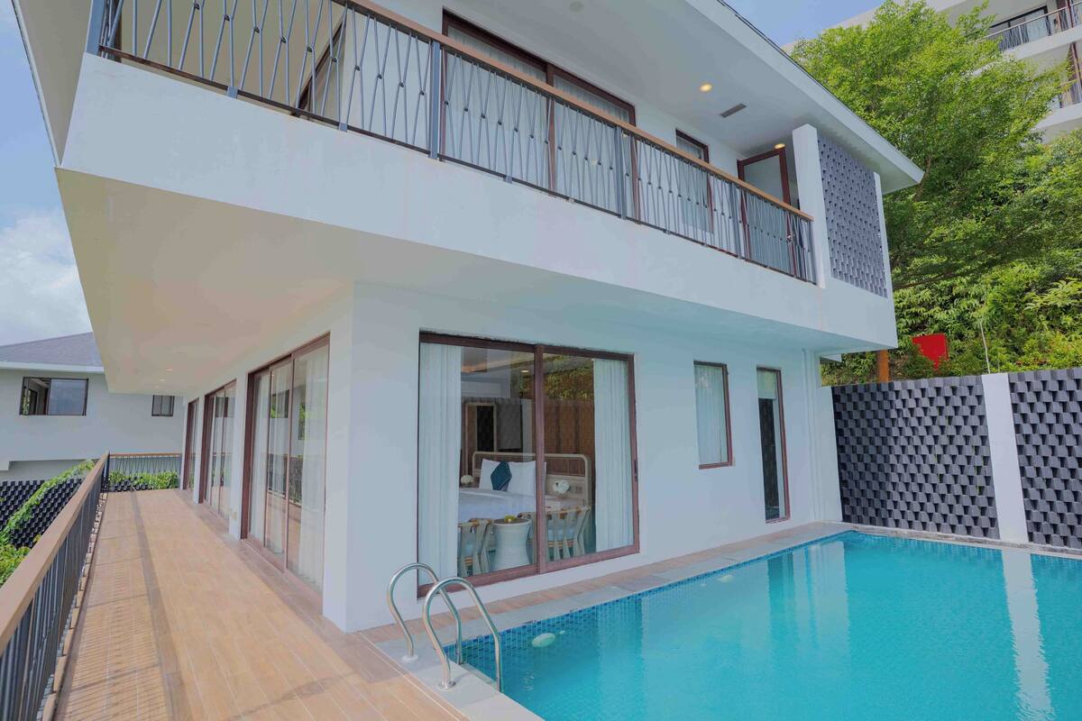 A modern two-story building with a swimming pool, large windows, and a balcony.