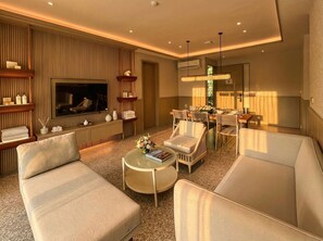A modern living room with a flat-screen TV, comfortable seating, a dining area with a chandelier, and a large window. - Riahi Villas by Swiss-Belhotel, Nirup Island (Nirup Island)