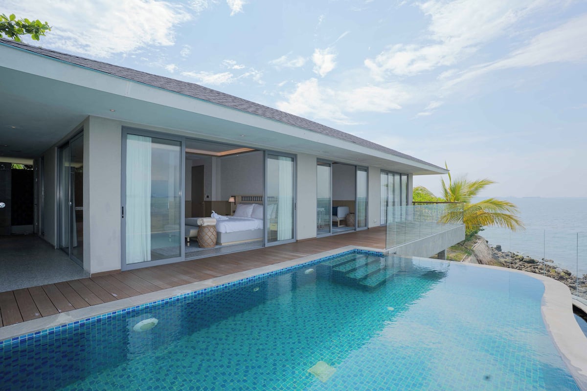 A modern house with a swimming pool, large glass doors, and a view of the sea.