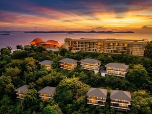 Egy üdülőkomplexum, amely több, kétszintes épületből, egy nagy, központi építményből áll, és ahonnan a tengerre nyílik kilátás a naplemente idején.
