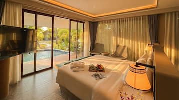 A hotel room with a bed, a TV, a bedside table with a lamp, and a view of a pool and greenery.