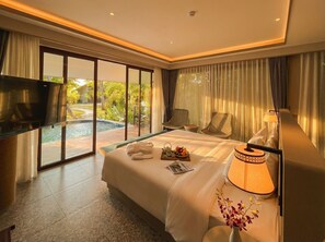 Una camera d'albergo con un letto, una televisione, un comodino con una lampada e vista su piscina e vegetazione.
