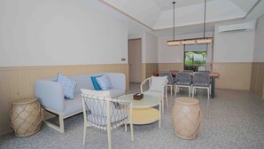 A modern lounge area with a sofa, chairs, a small table, and a drum. - Riahi Villas by Swiss-Belhotel, Nirup Island (Nirup Island)