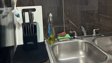 A kitchen with a stainless steel sink, a knife block, a bottle of dish soap, and a green cloth.