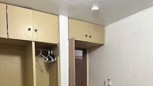 Ein Schlafzimmer mit einem Bett, einem Nachttisch mit Lampe, einem Kleiderschrank und einer Tür zu einem anderen Raum.