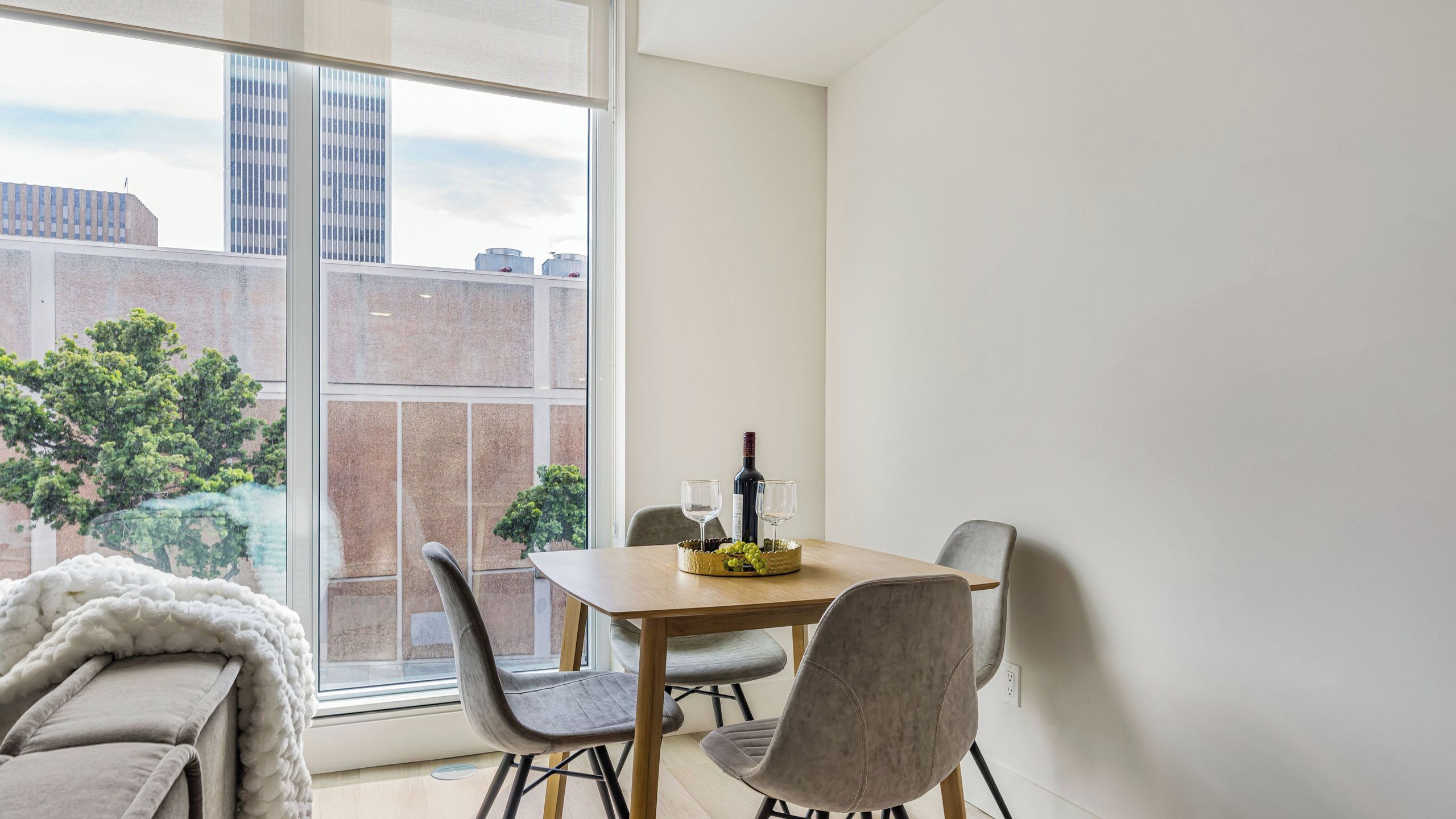 A dining area with a table, chairs, a bottle of wine, and a basket of grapes.