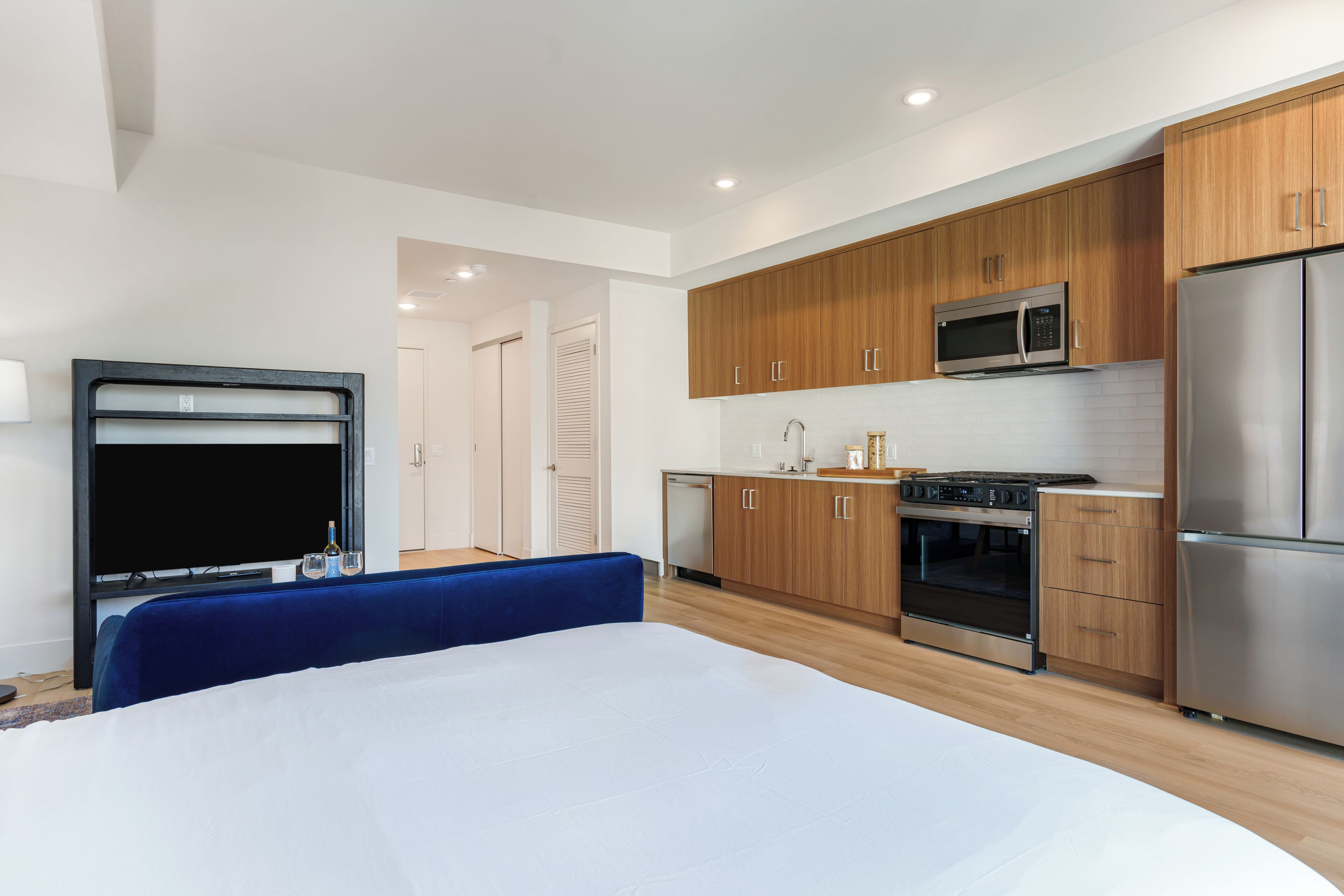 Ein modernes Hotelzimmer mit einem Bett, einem Fernseher, einer Küchenzeile inklusive Mikrowelle, Herd und Kühlschrank sowie einem Badezimmer mit Dusche und Toilette.