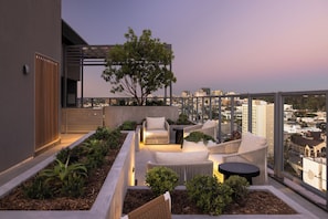 A rooftop terrace with a seating area, a tree, and a city view.