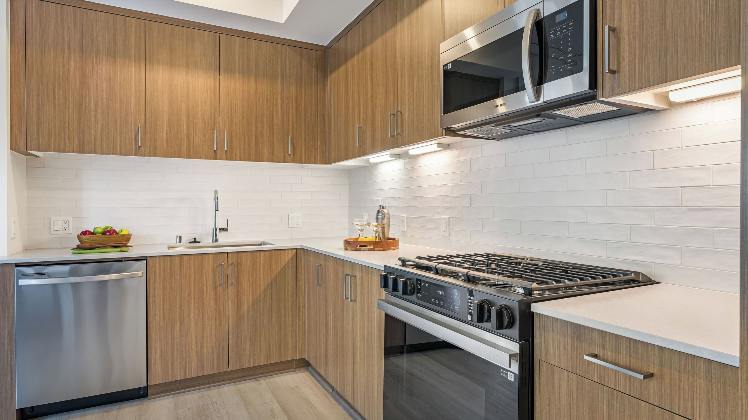 A modern kitchen with wooden cabinets, stainless steel appliances, and a white tiled backsplash.