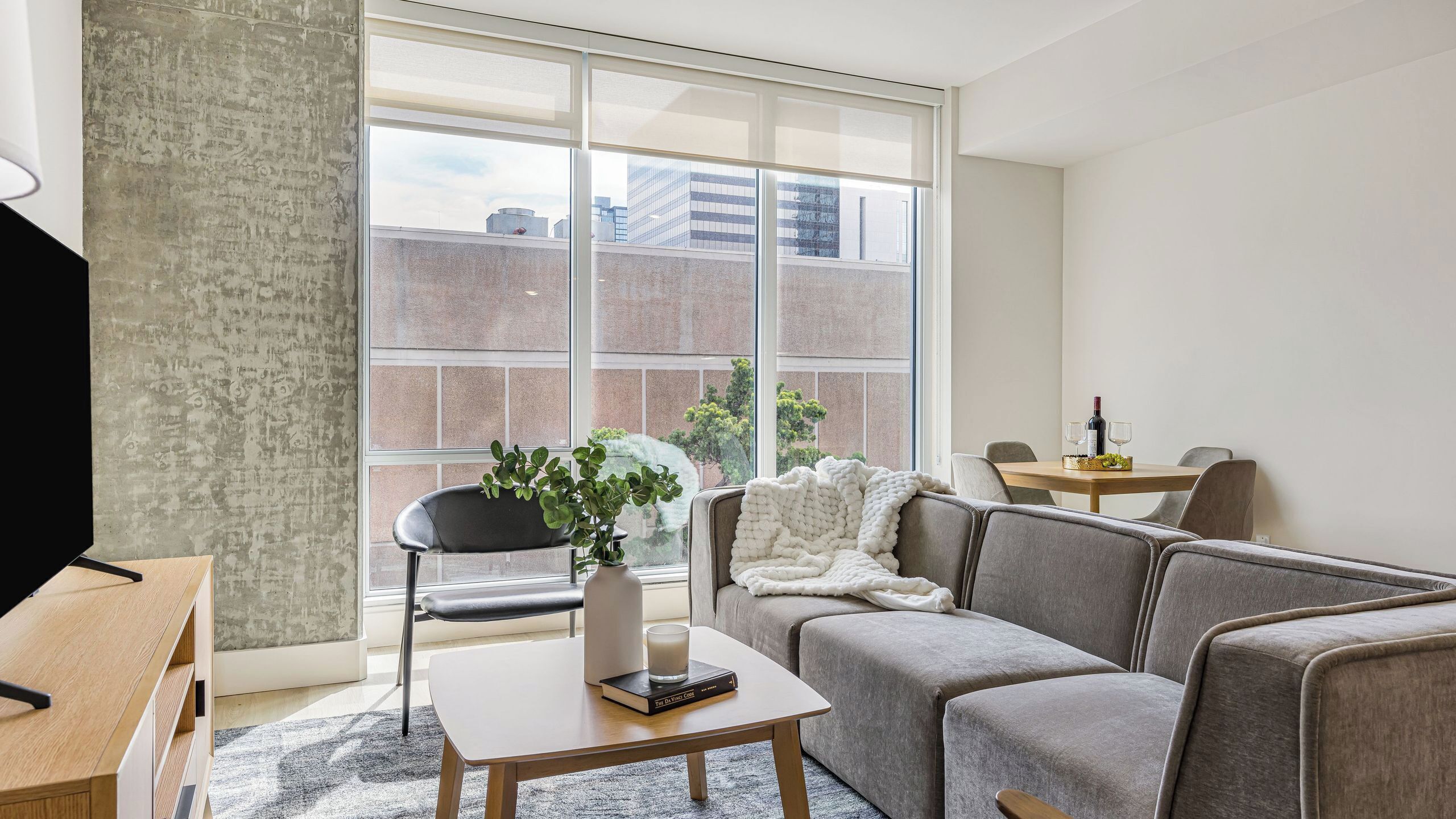 A modern living room with a sofa, a coffee table, a TV, and a large window with a city view.