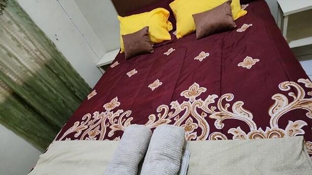 A neatly made bed with a patterned bedspread, two pillows, and two rolled towels. - Casa de 3-Cuartos de Dormitorios Con Aire AC Santa Ana (Santa Ana)