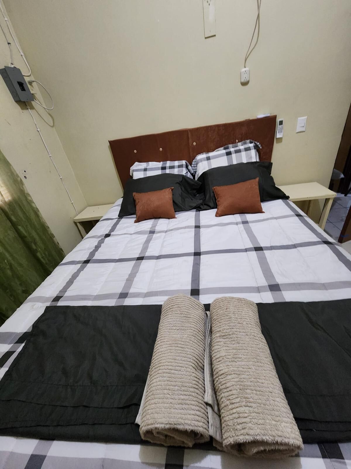 A bed with a checkered bedspread, two brown pillows, and two rolled towels.