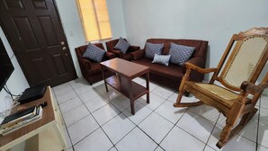 A living room with a brown sofa, a wooden chair, a small table, and a door. - Casa de 3-Cuartos de Dormitorios Con Aire AC Santa Ana (Santa Ana)