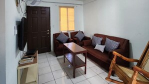 A small, well-lit living room with a sofa, a coffee table, a rocking chair, a TV, and a standing fan. - Casa de 3-Cuartos de Dormitorios Con Aire AC Santa Ana (Santa Ana)