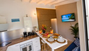 A modern kitchen with a dining area, a TV displaying a beach scene, and a sign on the wall. - Canopée Créole | House with a garden and a hot tub (Petit-Canal)