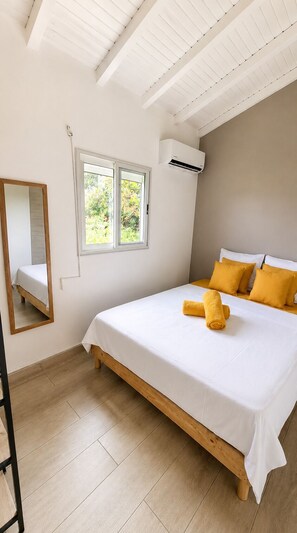 A bedroom with a bed, a window, an air conditioning unit, and a mirror. - Canopée Créole | House with a Garden and Hot Tub (Petit-Canal)