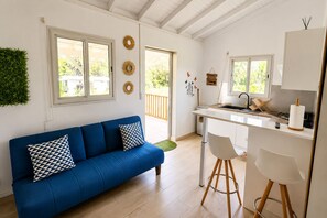 A modern kitchen with a white countertop, a blue sofa with patterned cushions, and a dining area with a white chair. - Canopée Créole | House with a garden and a hot tub (Petit-Canal)