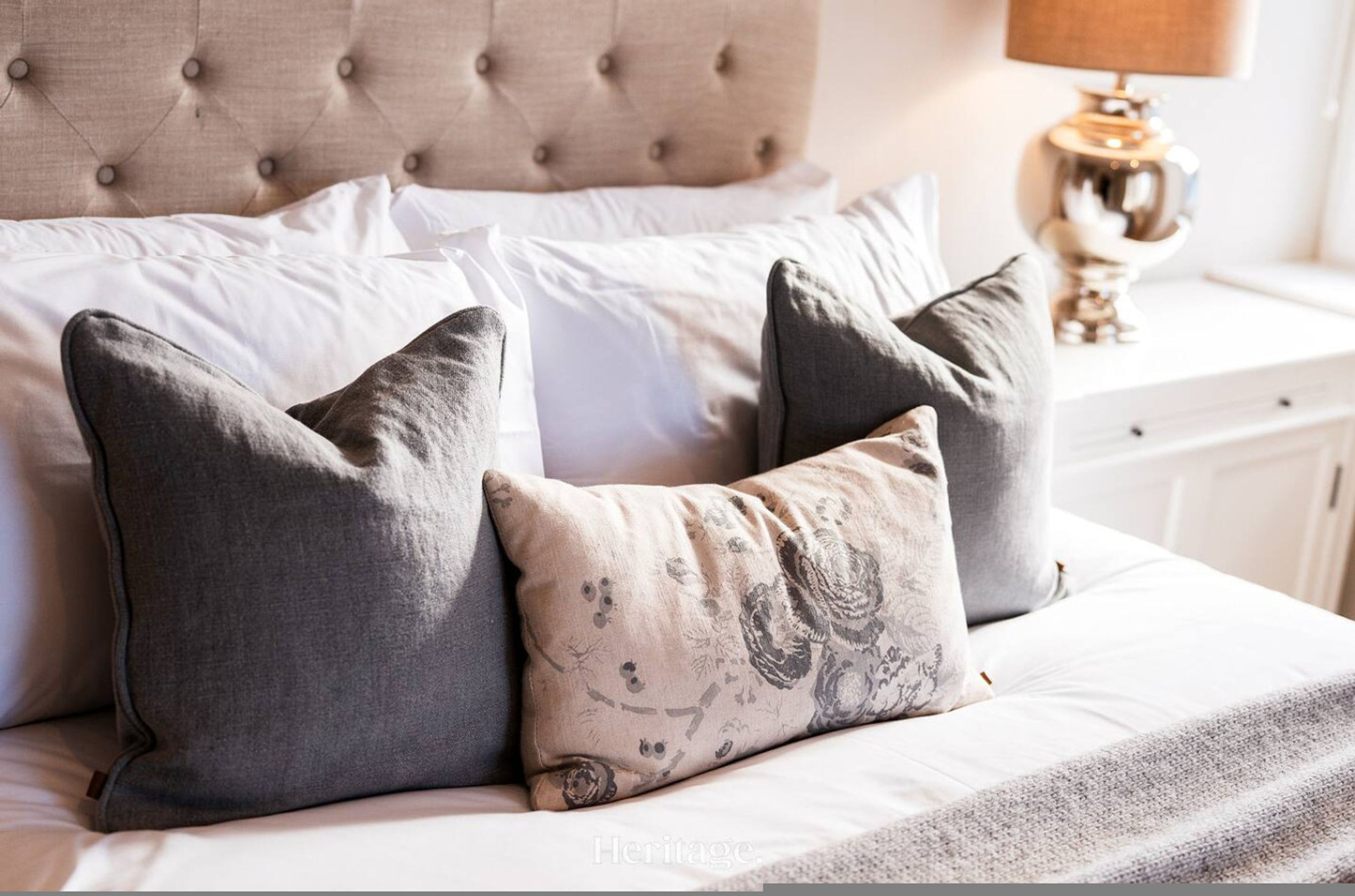 A bed with a tufted headboard, two pillows, and a bedside table with a lamp.