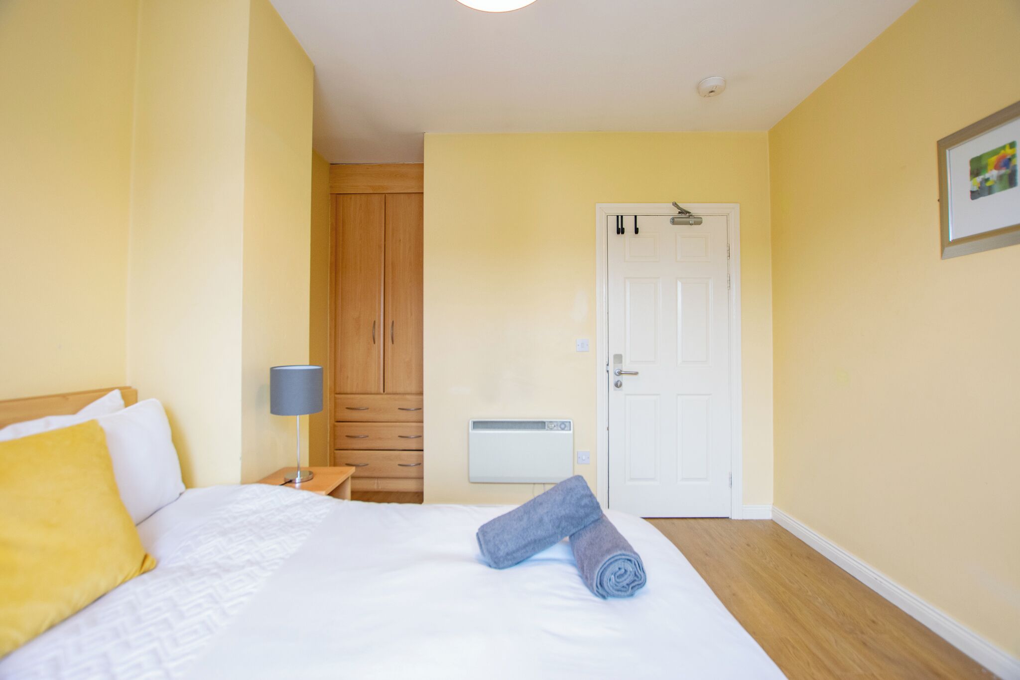 Una habitación de hotel con cama, mesita de noche, lámpara, armario y puerta.