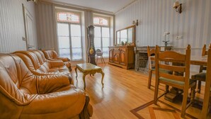 A living room with a leather sofa, wooden dining table, chairs, a clock, and a fireplace. - Léo - BAR SUR AUBE - Gîte (BAR SUR AUBE)