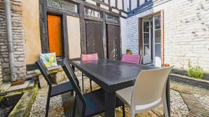An outdoor dining area with a table and chairs, a potted plant, and a building with exposed brick and timber framing. - Léo - BAR SUR AUBE - Gîte (BAR SUR AUBE)