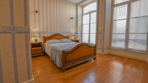 A bedroom with a wooden bed, two bedside tables with lamps, striped wallpaper, and large windows. - Léo - BAR SUR AUBE - Gîte (BAR SUR AUBE)