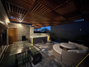 An outdoor patio with a glass table, wicker furniture, a stone wall, and a wooden ceiling. - Propiedad Para Pasarla Bien (Santo Domingo Este)
