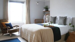 Ein Schlafzimmer mit Bett, Stuhl, Nachttisch, Lampe und einem Fenster mit Vorhängen.