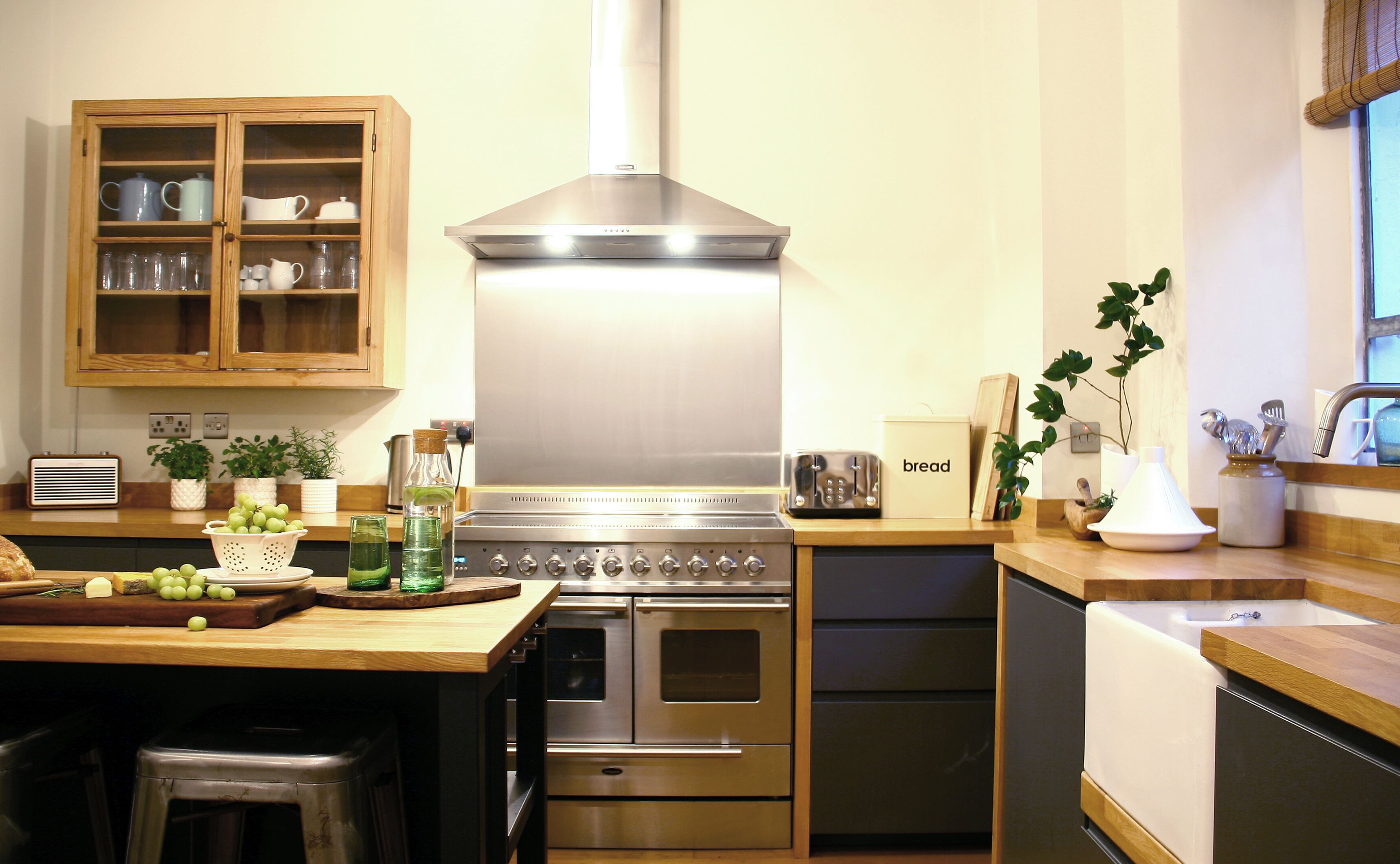 A modern kitchen with stainless steel appliances, wooden cabinets, and a central island with a cutting board and grapes.