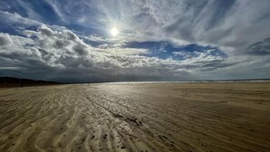 Ein weiter Sandstrand mit Fußspuren und ein klarer Himmel mit Wolken.