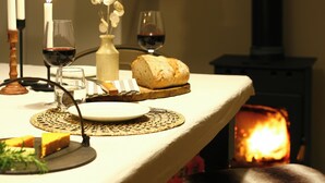 Ein gedeckter Tisch mit Brot, einem Glas Rotwein, einer Kerze und einer Vase mit Trockenblumen.