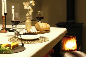 Ein gedeckter Tisch mit Brot, einem Glas Rotwein, einer Kerze und einer Vase mit Trockenblumen.
