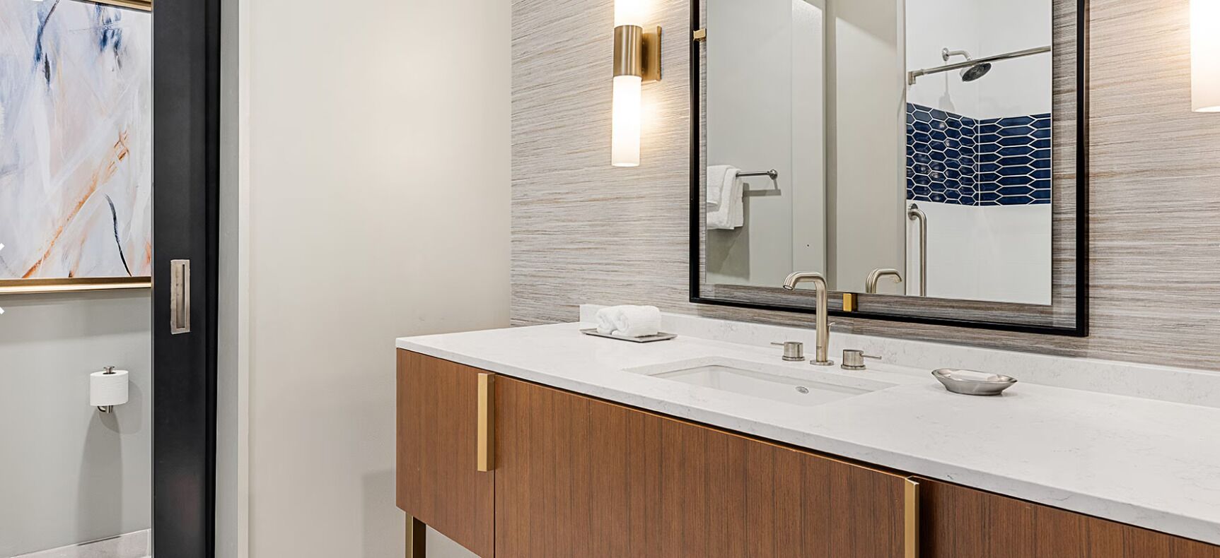 A modern bathroom with a large mirror, two sinks, a towel dispenser, and a wooden vanity.