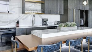 Une cuisine moderne dotée d’un îlot central, de meubles de couleur sombre et d’un coin repas avec des chaises en marbre.