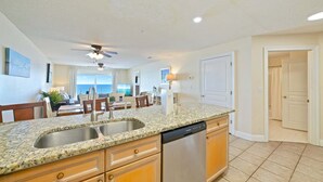 A kitchen with granite countertops, stainless steel appliances, wooden cabinets, and a ceiling fan. - Beautiful Beachfront 3BR Condo with Pool! FREE Summer Beach Service! (Destin)