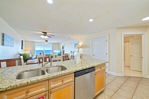 A kitchen with granite countertops, stainless steel appliances, wooden cabinets, and a ceiling fan. - Beautiful Beachfront 3BR Condo with Pool! FREE Summer Beach Service! (Destin)